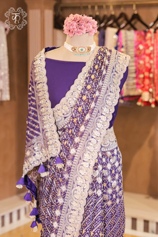 Bandhani Georgette Saree featuring an all-over bandhani print body, solid blouse, hanging pallu tassels, and a hand-embroidered scalloped zardozi border from Kridhaa.