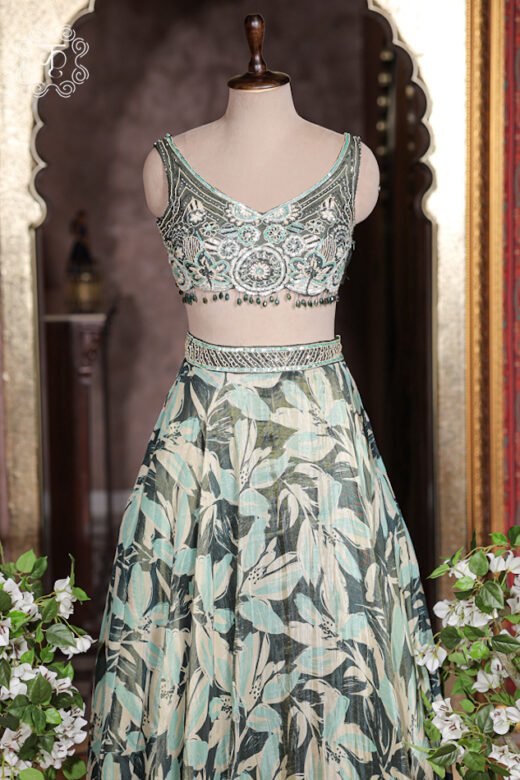 Sage green botanical leaf printed silk lehenga set with hand embroidered V-neck blouse on mannequin.