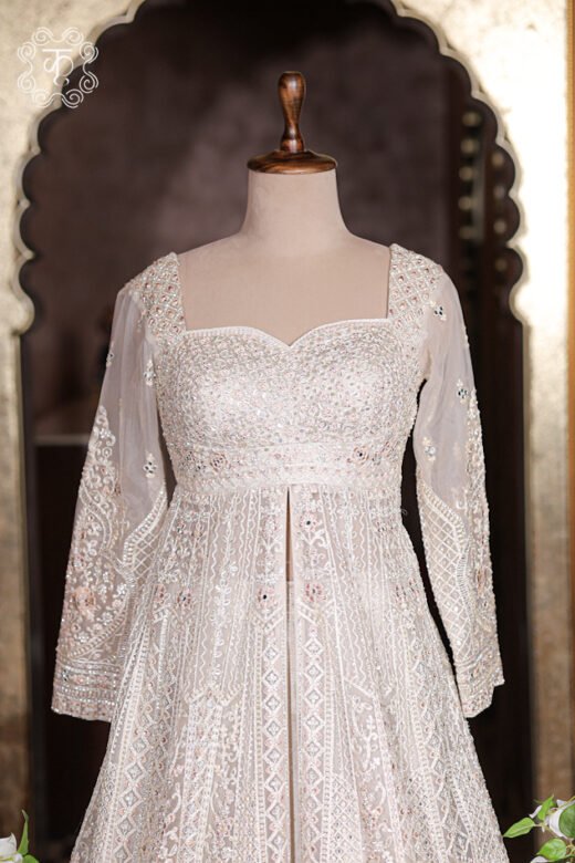 Front slit detail of embroidered jacket opening to reveal plain ivory silk lehenga skirt underneath.