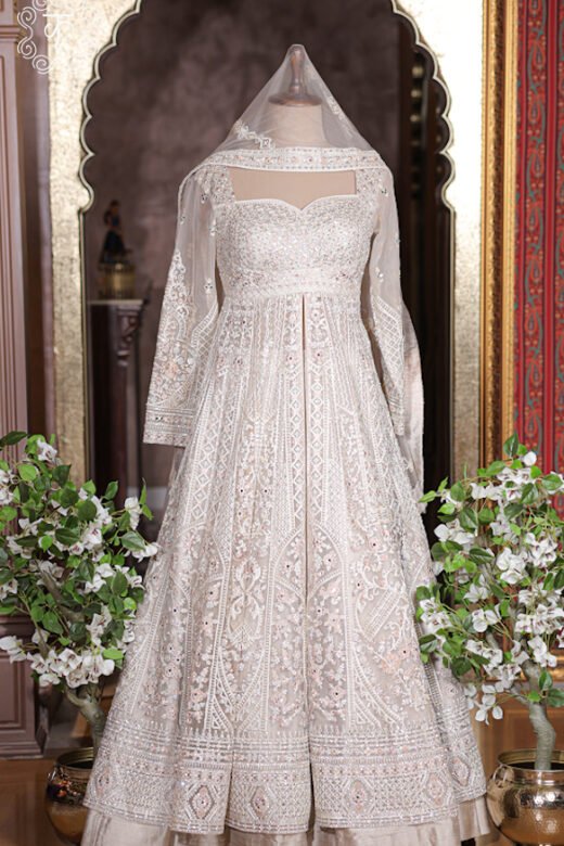 Ivory white heavily embroidered long jacket lehenga set with full sleeves on mannequin.