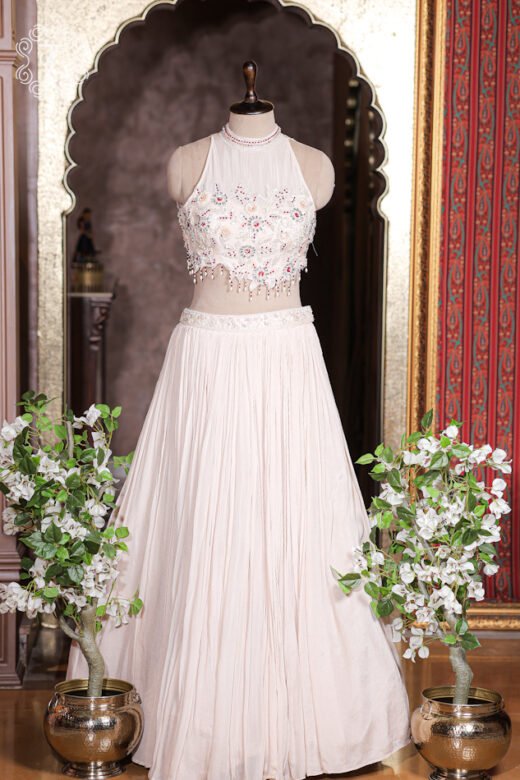 Pastel blush pink pleated georgette lehenga set with heavily embroidered halter neck blouse.