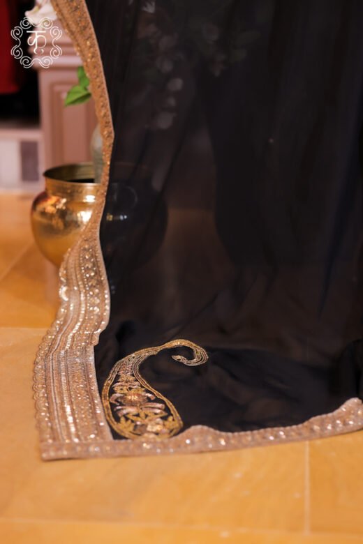 Close-up of black organza dupatta corner with gold zardozi embroidered paisley motif and sequin border