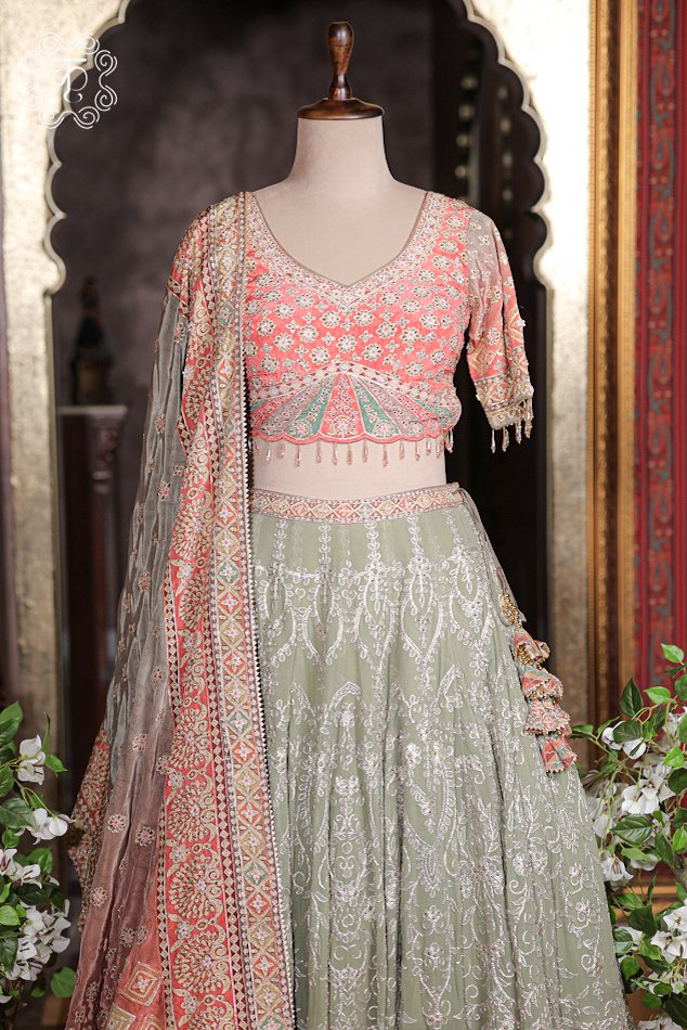 Detailed texture of sage green embroidered skirt layer parting over peach printed border and tassel latkans.