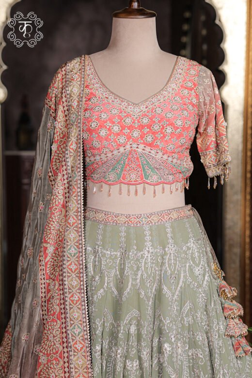 Close up of peach pink V-neck blouse with silver threadwork, mirror embroidery, scalloped green waist, and bead fringe.