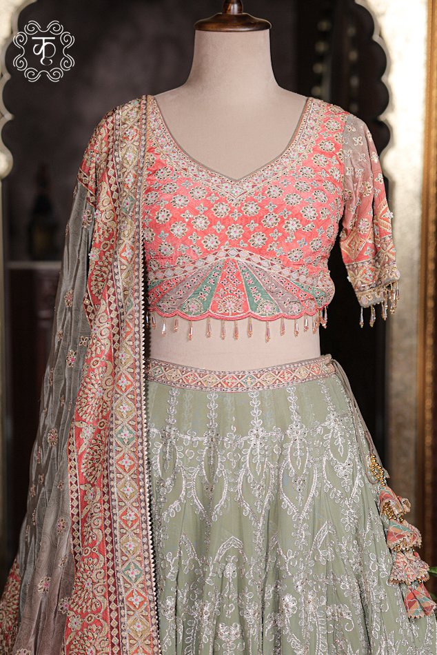 Close up of peach pink V-neck blouse with silver threadwork, mirror embroidery, scalloped green waist, and bead fringe.