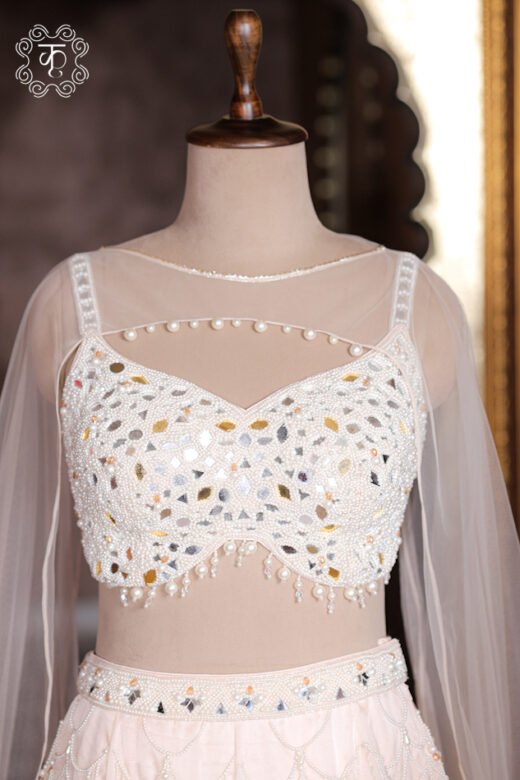 Sheer illusion neckline of ivory blouse with delicate pearl string detail across chest.