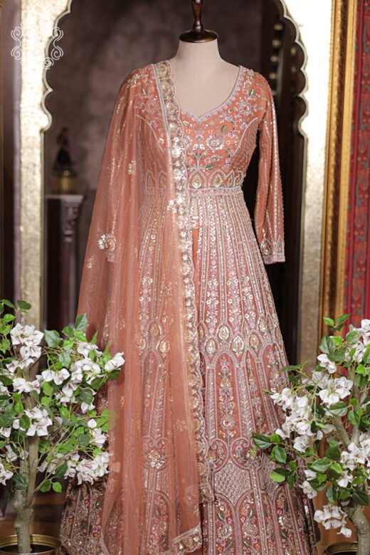 Rust orange heavily embroidered long jacket lehenga set with three quarter sleeves on mannequin.